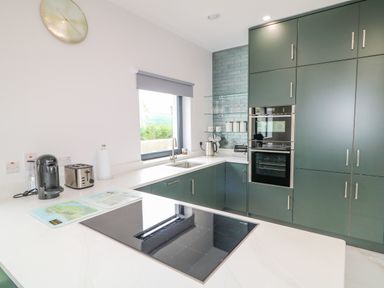 A kitchen with green cabinets a black cooktop a coffee machine a toaster and a window at Wee Andy's in Slavary near Buncrana County Donegal