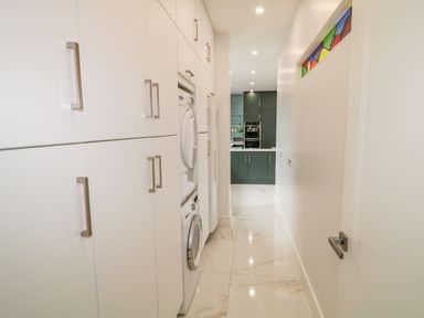 A hallway with white cabinets and stacked washing machines leading to a kitchen with grey cabinets at Wee Andy's in Slavary near Buncrana County Donegal