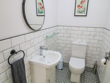 A bathroom with a sink, toilet, round mirror, towel ring with a towel, and a framed picture at Wee Andy's Slavary near Buncrana County Donegal