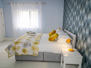 A bedroom with a bed yellow and gray floral blanket yellow round pillows a white bedside table and an orange lamp at Wee Andy's Slavary near Buncrana County Donegal