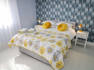 A bedroom with a bed covered with a floral quilt and yellow pillows and two bedside tables with lamps at Wee Andy's Slavary near Buncrana County Donegal