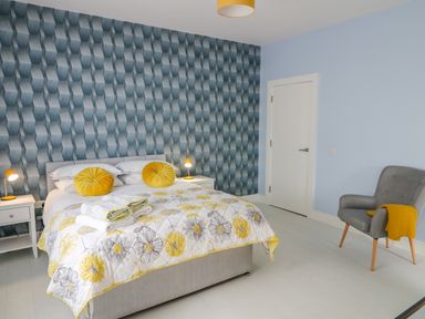 A bedroom with a bed and yellow cushions a blue patterned wall and a gray chair with a yellow blanket at Wee Andy's Slavary near Buncrana County Donegal