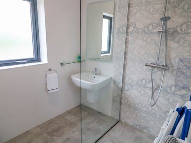 A bathroom with a wall-mounted sink a mirror shower with a glass partition and a window at Wee Andys Slavary near Buncrana County Donegal