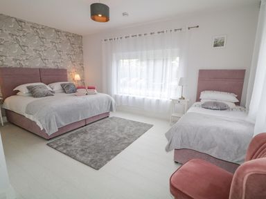 A bedroom with a double bed a single bed a window with white curtains a bedside table and a red chair at Wee Andy's in Slavary near Buncrana County Donegal