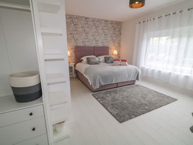 A bedroom with a large bed bedside tables a grey rug and a window with sheer curtains at Wee Andy's Slavary near Buncrana County Donegal