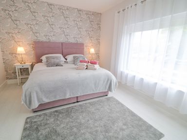 A bedroom with a double bed with a pink headboard bedside tables with lamps and a gray rug on the floor at Wee Andy's Slavary near Buncrana County Donegal