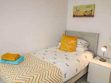 A single bed with yellow and blue towels on a patterned blanket and a bedside table with a lamp at Wee Andy's in Slavary near Buncrana County Donegal
