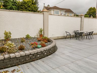 A patio area with tiled floor a raised garden bed with small plants and a table with chairs against a white wall at Wee Andy's Slavary near Buncrana County Donegal