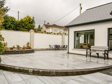A backyard patio with grey tiles a bench a table and chairs and a raised garden bed at Wee Andy's Slavary near Buncrana County Donegal