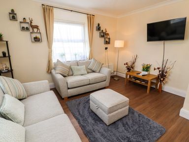 A living room with two sofas a footstool a rug a coffee table a wall-mounted television and decorative shelves at Neland View in Windermere