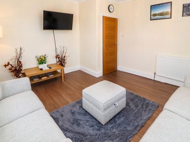 A living room with two sofas a gray ottoman on a gray rug a wall mounted television a wooden table with decorations and a wooden door at Neland View in Windermere