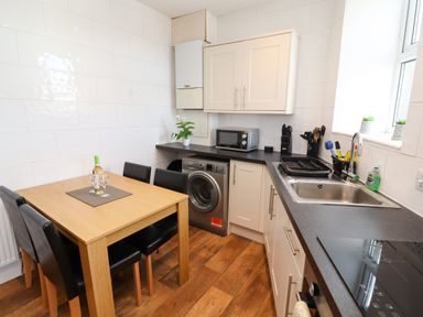 A kitchen with a wooden dining table and four black chairs a washing machine microwave sink and cooking utensils at Neland View in Windermere