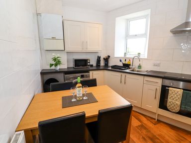 A kitchen with wooden table and black chairs with a bottle and glasses on the table at Neland View in Windermere
