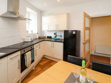 A kitchen with white cabinets black countertops a black refrigerator and a wooden dining table with a bottle and glasses at Neland View in Windermere