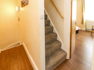A hallway with carpeted stairs and wooden flooring leading to a room with a bed and chair at Neland View in Windermere