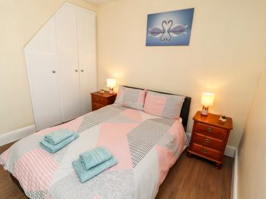 A bedroom with a double bed two wooden bedside tables with lamps wall art of two swans and a built-in white wardrobe at Neland View in Windermere