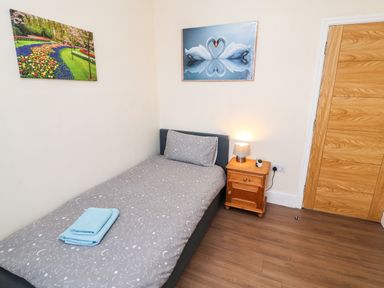 A bedroom with a single bed and gray bedding a wooden nightstand with a lamp and door with wooden panels at Neland View in Windermere