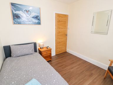 A bedroom with a single bed bedside table with lamp wooden door wall mirror and a picture of swans at Neland View in Windermere
