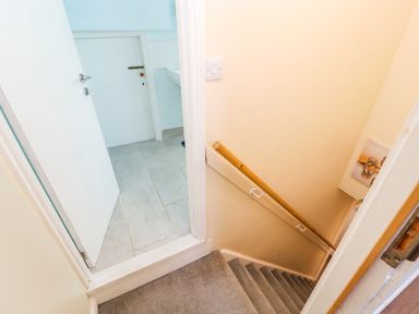 Staircase with carpeted steps and wooden handrail leading down from a landing with tile floor and open door at Neland View in Windermere