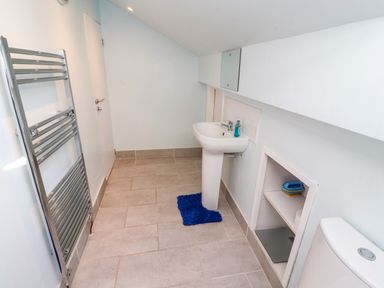 A bathroom with a pedestal sink a blue rug a chrome towel warmer and a small built in shelf at Neland View in Windermere
