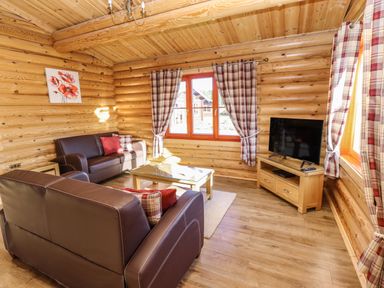 A living room with leather sofas a glass coffee table a television on a wooden stand and plaid curtains at Elm Lodge in Greetham Rutland