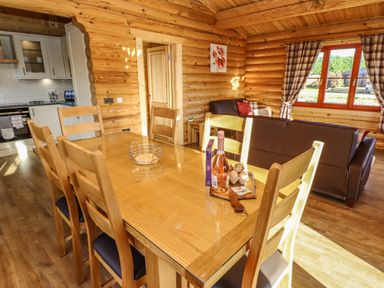 A dining area with a wooden table and chairs next to a kitchen and a seating area with sofas at Elm Lodge in Greetham Rutland