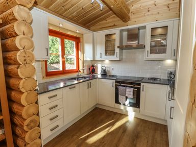 A kitchen with white cabinets black countertop wooden ceiling and floors and an orange window frame at Elm Lodge in Greetham Rutland