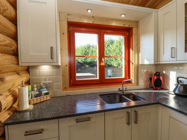A kitchen corner with a double sink under an orange window with white cabinets and black countertop at Elm Lodge in Greetham Rutland