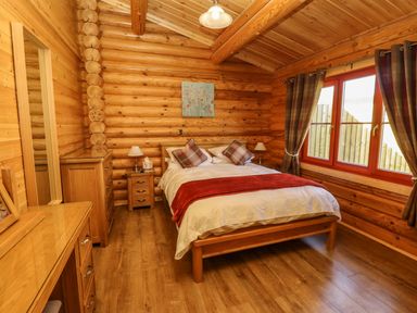 A bedroom with a wooden bed and furniture and a window with curtains at Elm Lodge in Greetham Rutland