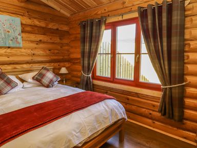 A bedroom with a bed white bedding and red throw next to a window with plaid curtains at Elm Lodge in Greetham Rutland