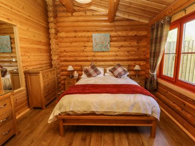 A bedroom with a wooden double bed two bedside tables with lamps a chest of drawers and a window with curtains at Elm Lodge in Greetham Rutland