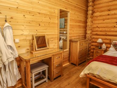 A bedroom with wooden walls containing a dressing table with mirror a stool a chest of drawers a bedside table with lamp and bed at Elm Lodge in Greetham Rutland