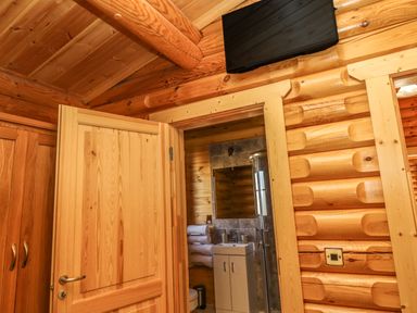 A wooden interior showing a door partially open to a bathroom with a sink towels and a shower at Elm Lodge in Greetham Rutland