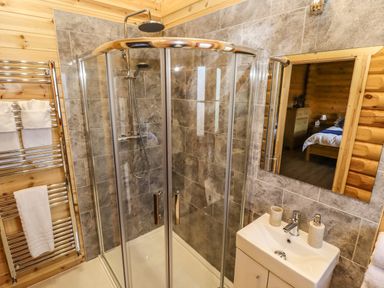 A bathroom with a glass shower enclosure a sink with soap dispensers a towel rack with towels and a mirror reflecting a bedroom at Elm Lodge Greetham Rutland