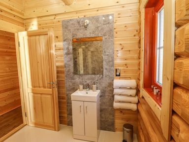 A bathroom with wood-paneled walls a white sink cabinet a mirror towels on a rack and a window at Elm Lodge in Greetham Rutland