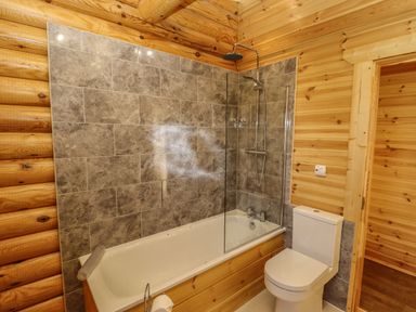 A bathroom with a bathtub shower combination a toilet and wooden walls at Elm Lodge in Greetham Rutland