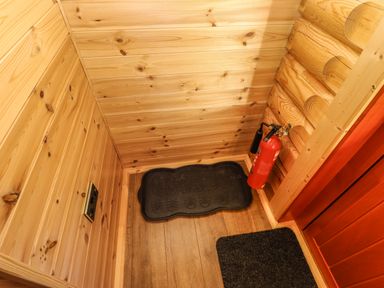 A corner with wooden walls and floor with a fire extinguisher and black boot tray at Elm Lodge in Greetham Rutland