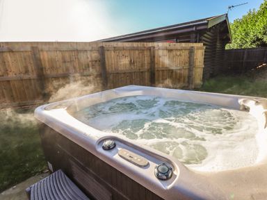 An outdoor hot tub with bubbling water next to a wooden fence and wooden cabin at Elm Lodge in Greetham Rutland