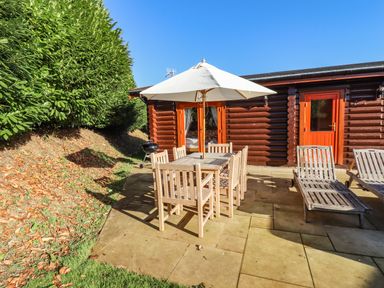 An outdoor patio area with a wooden dining table and chairs under a white umbrella next to a log cabin at Elm Lodge in Greetham Rutland