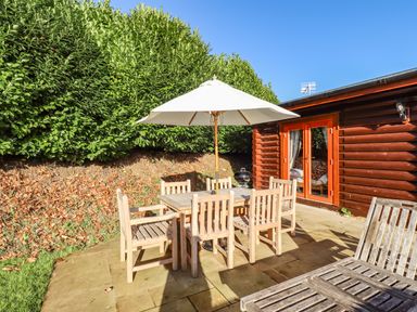 An outdoor patio with a wooden dining table and chairs under a large umbrella next to a wooden building at Elm Lodge in Greetham Rutland