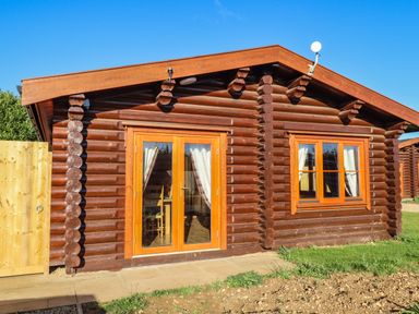 A wooden log cabin with glass double doors and a window with curtains at Elm Lodge in Greetham Rutland
