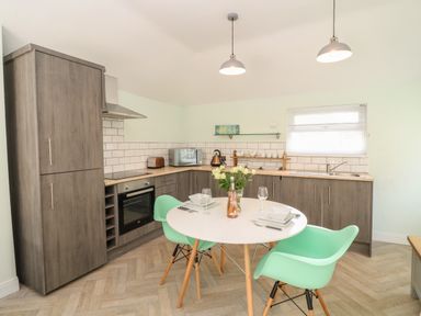 A kitchen with wooden cabinets a round dining table and green chairs at Byghan Thornton in Illogan