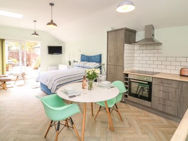 A kitchen and bedroom area with a dining table and two chairs at Byghan Thornton in Illogan