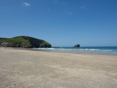 A sandy beach with people near the water and a rocky hill in the background at Byghan Thornton in Illogan