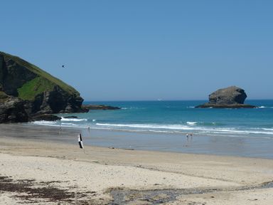 A beach with people walking on the shore cliffs on the left and a rock formation in the sea at Byghan Thornton in Illogan