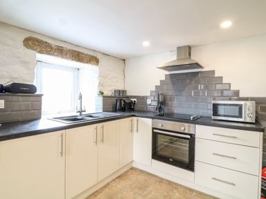 A kitchen with white cabinets black countertop gray subway tile backsplash oven microwave and stainless steel sink at Polgear View in Polgear Nr Redruth