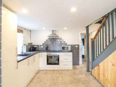 A kitchen with white cabinets grey tiled backsplash oven and wooden staircase at Polgear View in Polgear Nr Redruth