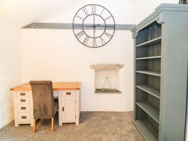 A room with a desk chair bookshelf wall clock and a niche with a glass bottle at Polgear View Polgear Nr Redruth