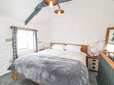 A bedroom with a large bed a wooden headboard bedside tables a window with curtains and a mirror at Polgear View Polgear Nr Redruth