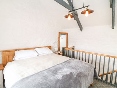 A bedroom with a wooden bed frame white pillows beige and gray blankets a wooden mirror and railing at Polgear View in Polgear Nr Redruth